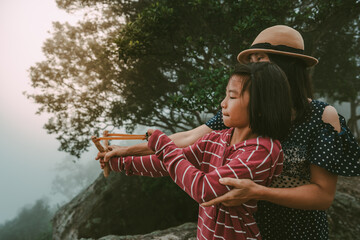 Children and mother holding slingshot for shooting seed of plants to forest on foggy and sky morning background 