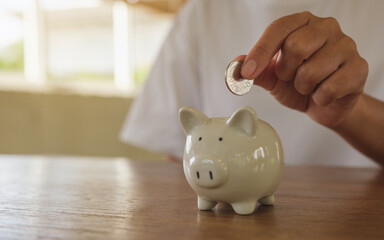 Closeup image of a woman putting coin into piggy bank for saving money concept