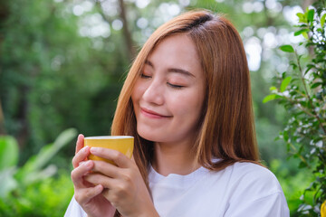 Portrait image of a beautiful young asian woman holding and drinking hot coffee in the outdoors