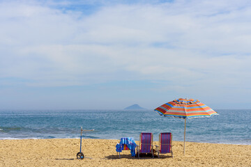 duas cadeiras de praia, um guarda sol e um carrinho de transporte sobre a areia da linda praia de...