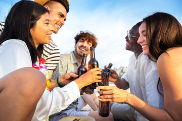 Close up of happy, diverse group of friends toasting with beer together at the beach. Multiracial people having fun.