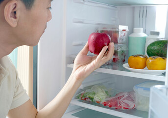 A man opens a refrigerator and he carries a red apple as a healthy food. Stay healthy by eating...
