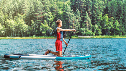 Teenager on a SUP board rakes a wave with an oar. SUP surfing. The concept of an active lifestyle.