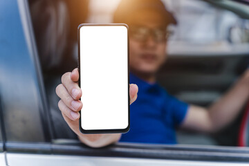 A mechanic in a blue uniform holds a mobile phone with a blank white screen and an approval. Repair in a car repair shop, car maintenance services.