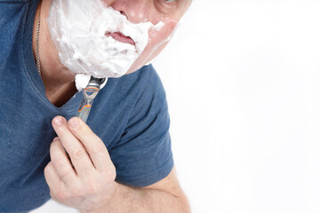 A man face in shaving foam shaves with a safety razor - 516110482