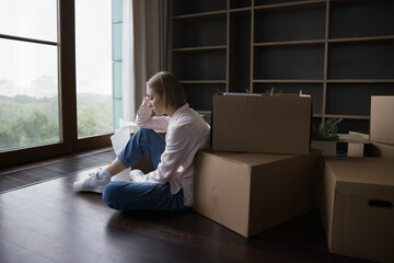 Sad lonely young renter woman moving out from home, sitting at pole of stacked paper boxes on...