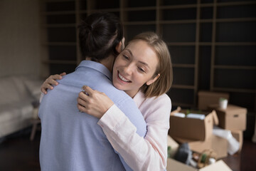 Happy thankful young woman embracing husband, boyfriend with love, gratitude at open paper boxes, moving into new apartment, celebrating relocation, home buying. Real estate purchase concept