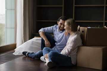 Joyful happy young couple taking break at paper boxes, enjoying leisure after moving, relocation into new home, smiling, laughing, discussing shipping, transportation service. Apartment buying concept