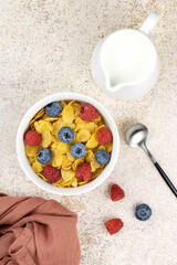 Corn flakes in a bowl with berries, milk on a beige background, top view. Breakfast with corn flakes and milk.