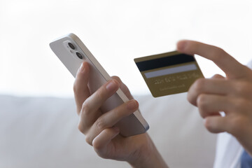 Close up female hands holds credit card and smartphone, pay bills on-line, using secure electronic...