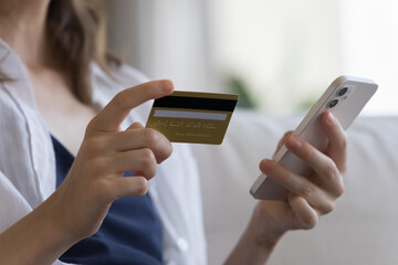 Close up cropped shot unknown female hands holds credit card and smartphone, make secure electronic payment, spend money, buying goods, e-services, do shopping at home. Safe e-pay, e-bank app concept