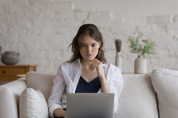 Attractive pensive young freckled woman sit on couch studying or working on-line use laptop. Freelance, e-learn, young generation and modern wireless tech, internet connection usage, education concept