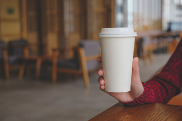 Woman hand holding white paper cup of hot coffee in coffee cafe.