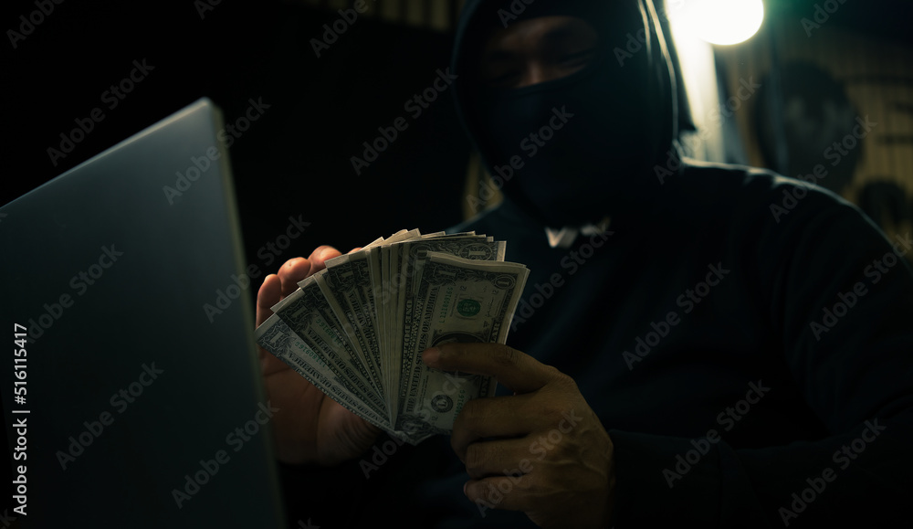 Wall mural Hands of a man in a hoodie holding money and using a laptop digging into financial data-Internet theft concept - Wall murals