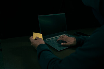 Hand of a man in a hoodie holding credit and using a laptop to hack credit card financial...