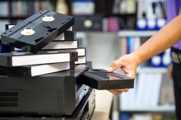 Close-up hand chooses and put or insert video cassette tape VHS on video tape player concept of...