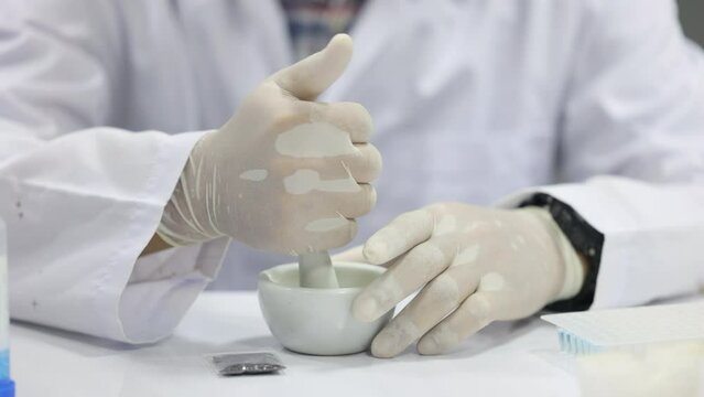 Doctor crushes pills into powder in lab.