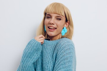 a close-up photo of a cute, emotional blonde woman standing in a blue sweater on a light background, winking funny looking at the camera
