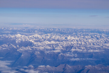 Window view from an airplane on the snow capped mountain ranges of the Alps at the border Austria Italy, Europe, EU. High peak are shrouded in clouds. Flying high above the ground. Freedom