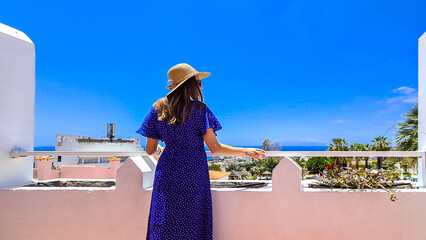 Rear view on tourist woman in summer hat and blue dress on a balcony on a luxury resort hotel on...