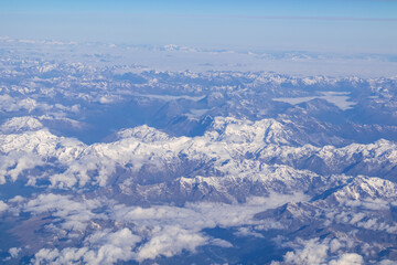Window view from an airplane on the snow capped mountain ranges of the Alps at the border Austria Italy, Europe, EU. High peak are shrouded in clouds. Flying high above the ground. Freedom