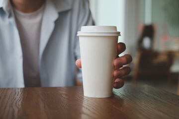Hand holding paper cup of hot coffee in cafe.