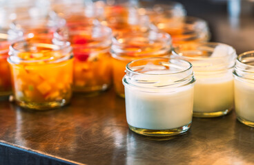 Homemade plain yogurt in small bottle glass on stainless steel shelf with blurred background of fruit salad in small bottle glass, close up image with warm light.