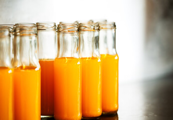 Fresh orange juice in small glass bottles, group of fresh orange juice in small containers on stainless steel shelf, blank space for text and design.