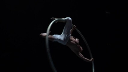 Muscular circus artist perform Cyr Wheel on a black background. Concept of desire, will and potential 