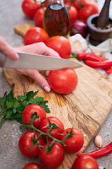 woman making notch on a tomato on wooden cutting board on grey kitchen concrete or stone table