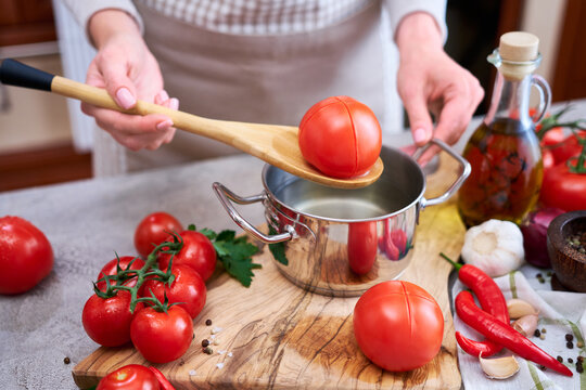 woman blanching a tomato holding over pan with hot water for further peeling