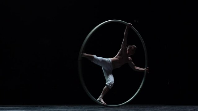 Muscular circus artist perform Cyr Wheel on a black background stage