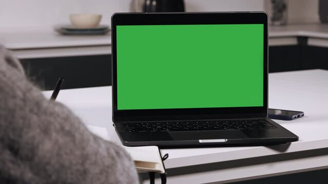 person writing notes learning online course on the desk laptop with green screen remote education for adults