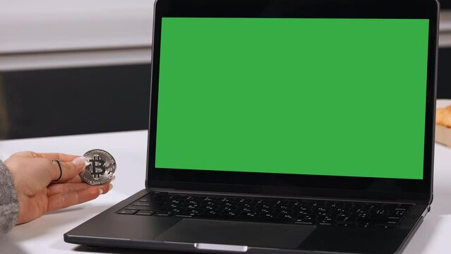 crypto online trader working at home laptop with green screen on the table in kitchen
