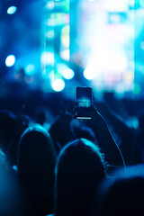 Using a smartphone in a public event, live music festival. Holding a mobile phone in hands and shooting photo or video content. Youth, party, vacation concept.