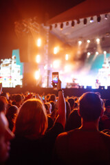 Plakat Using a smartphone in a public event, live music festival. Holding a mobile phone in hands and shooting photo or video content. Youth, party, vacation concept.