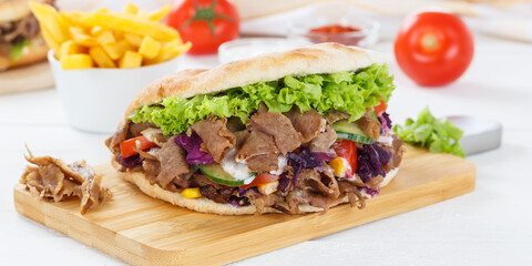 Döner Kebab Doner Kebap fast food meal in flatbread with fries on a kitchen board panorama