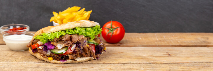 Döner Kebab Doner Kebap fast food meal in flatbread with fries panorama on a wooden board and copyspace copy space