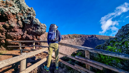 Active Man with backpack standing on fence at the edge of active volcano crater of Mount Vesuvius, Province of Naples, Campania, Italy, Europe, EU. Person enjoying the view on the mountain summit. Awe © Chris