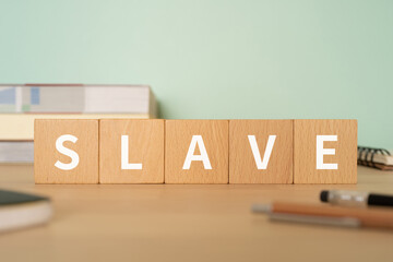 奴隷のイメージ｜「SLAVE」と書かれたブロックが置かれたデスク
