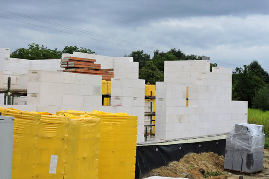 A house under construction, walls made of acc blocks, rough windows and door openings, reinforced brick lintels, a scaffolding, insulated foundation walls, solid concrete blocks and acc blocks