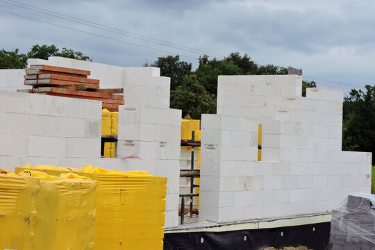 A house under construction, walls made of acc blocks, rough windows and door openings, reinforced brick lintels, a scaffolding, insulated foundation walls, solid concrete blocks and acc blocks