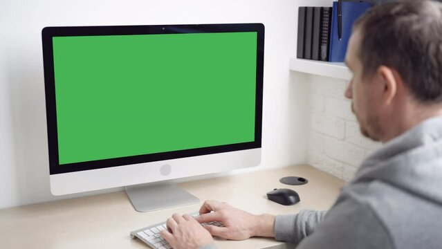 man sitting at the workplace typing on keyboard computer with green screen minimalist workplace at home or office
