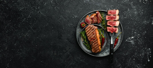 grilled marbled beef steaks striploin on a fork. On a black stone background.