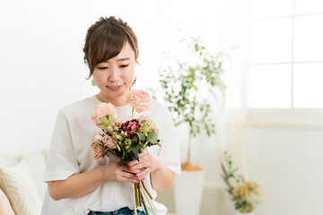 家のソファで花束を持つ日本人女性（母の日・誕生日・結婚記念日）
