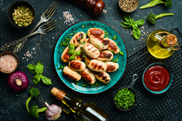 Grilled sausages with rosemary and spices on a plate. Barbecue. Meat menu. Top view. On a stone background.