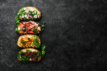 Set of colored sandwiches with tomatoes, prosciutto, vegetables and cheese on a black stone background. Bruschetta. Top view.