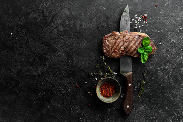 Grilled rib eye steak, herbs and spices. On a black stone background.