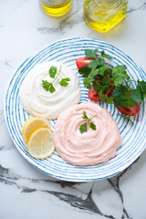 Plate with beige and pink taramasalata or greek traditional fish roe salad, elevated view on a black and white marble background