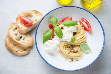Plate of spaghetti and stracciatella or cheese produced from italian buffalo milk, horizontal shot on a grey stone background